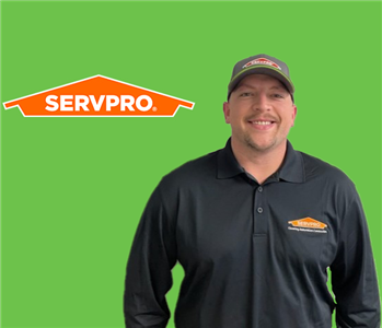 SERVPRO employee with hat and wearing a black shirt in front of a green background