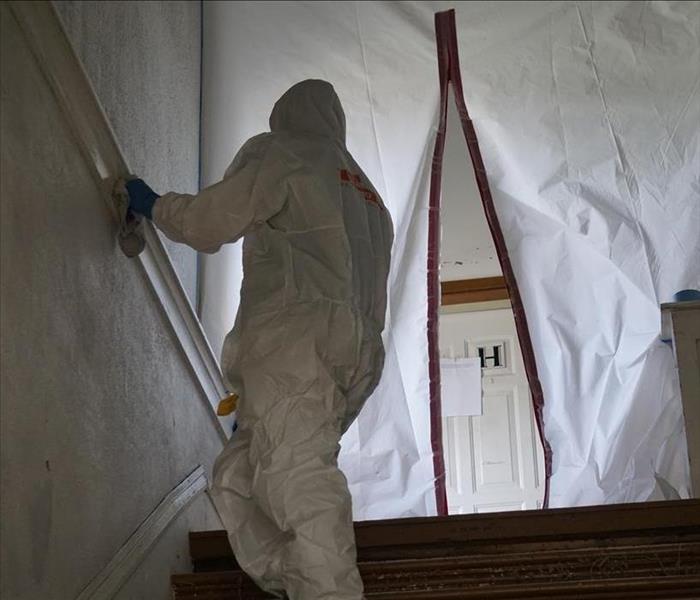 A man in a tyvek suit cleaning a wall